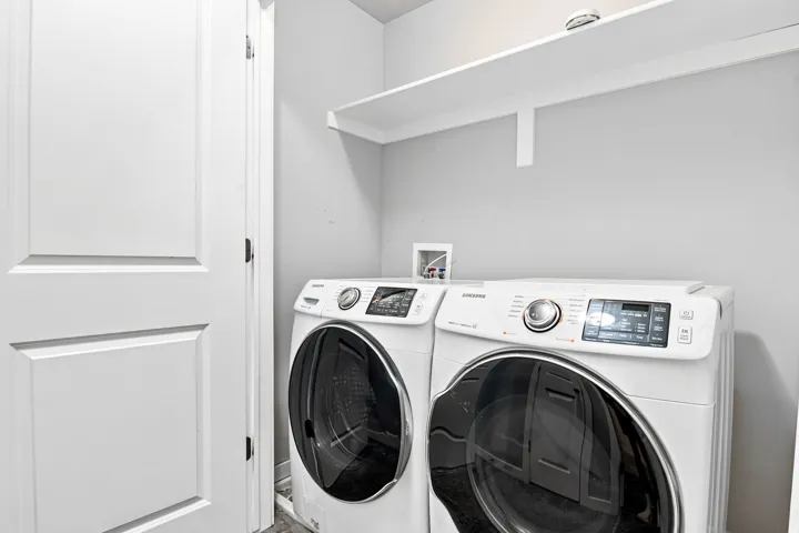 Dedicated laundry area featuring a white bi-fold door, a white wall-mounted shelf, and light gray painted walls