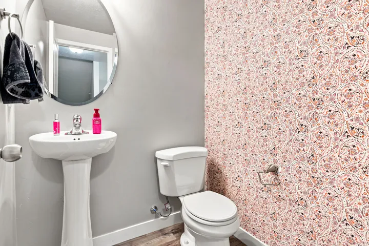 Bathroom featuring a pedestal sink, round mirror, toilet, and a patterned accent wall