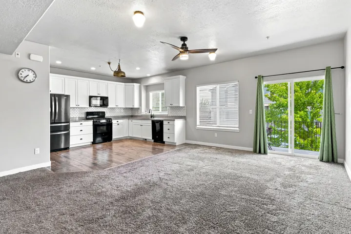 Open-concept living area featuring a kitchen with white cabinetry, dark countertops, and black appliances