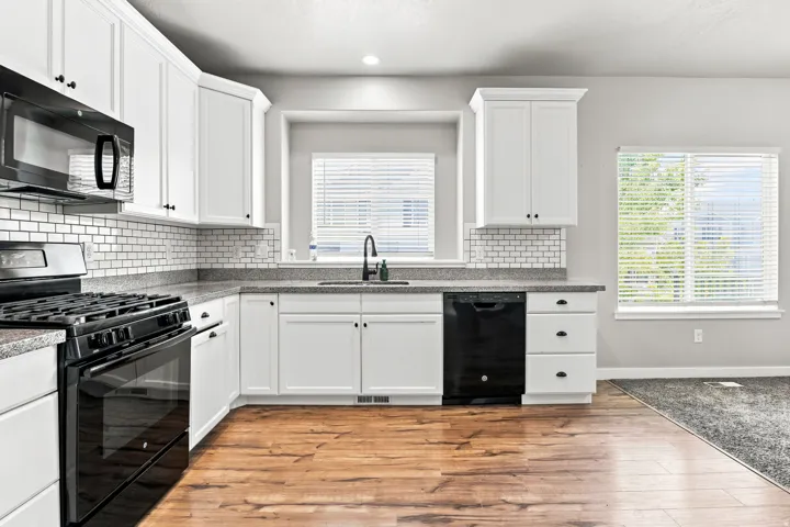 Kitchen featuring white cabinetry, dark speckled countertops, a subway tile backsplash, and wood-finish flooring