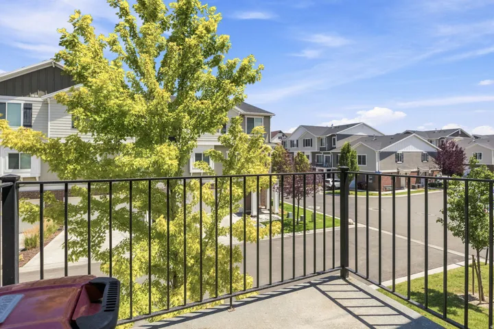 Concrete balcony off of family room, with black metal railing, offering views of a residential street and multi-story townhomes