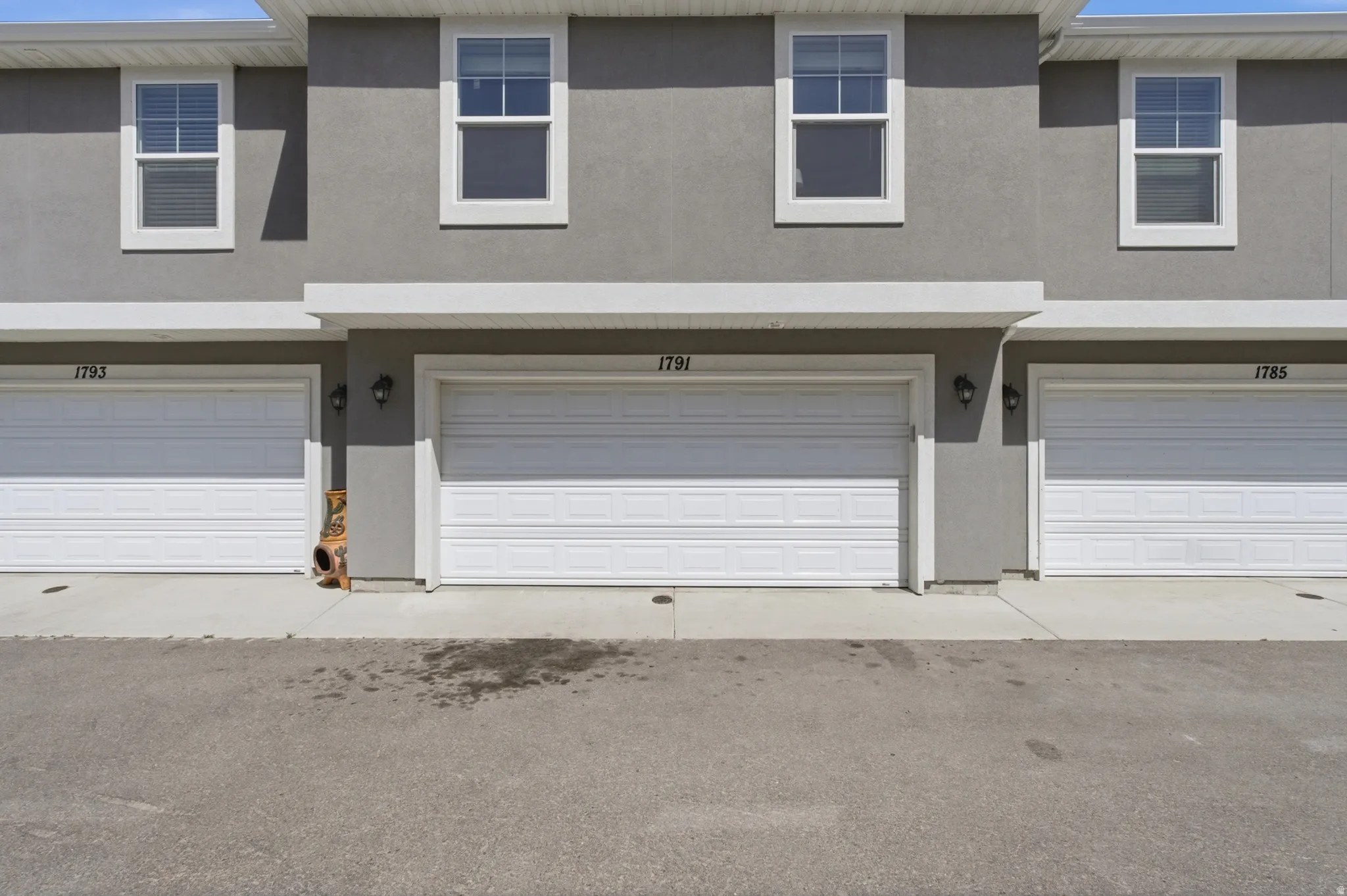 Gray stucco exterior featuring white framed windows with blinds, white garage doors, and exterior lighting fixtures