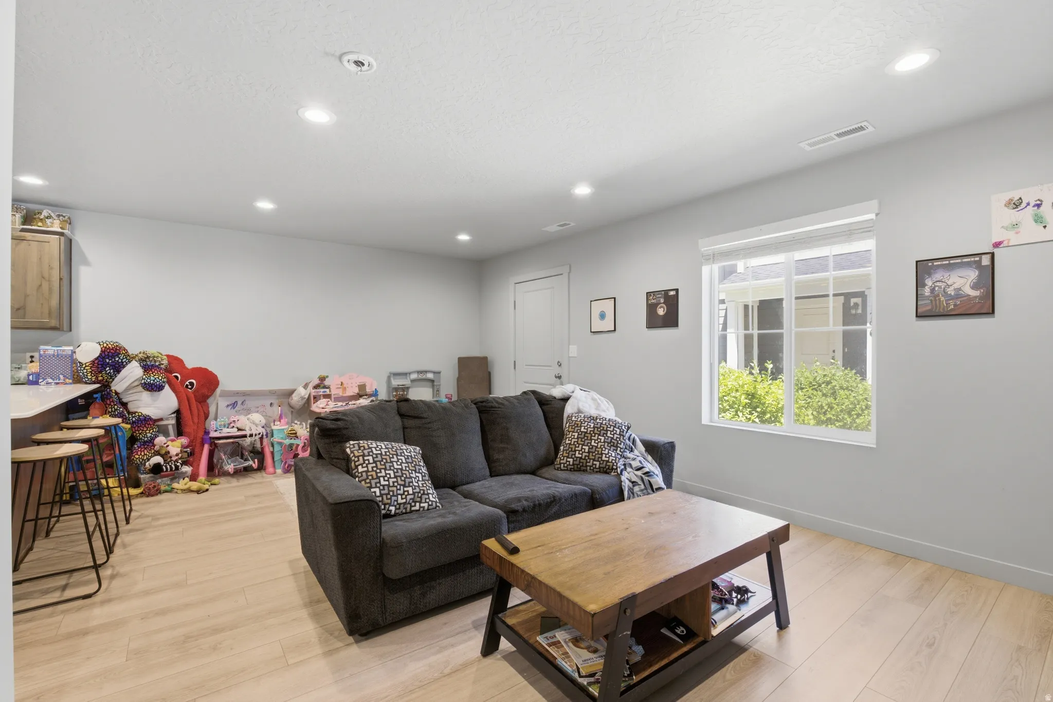 Open-concept living area featuring light wood-finish flooring, recessed lighting, and a white framed window
