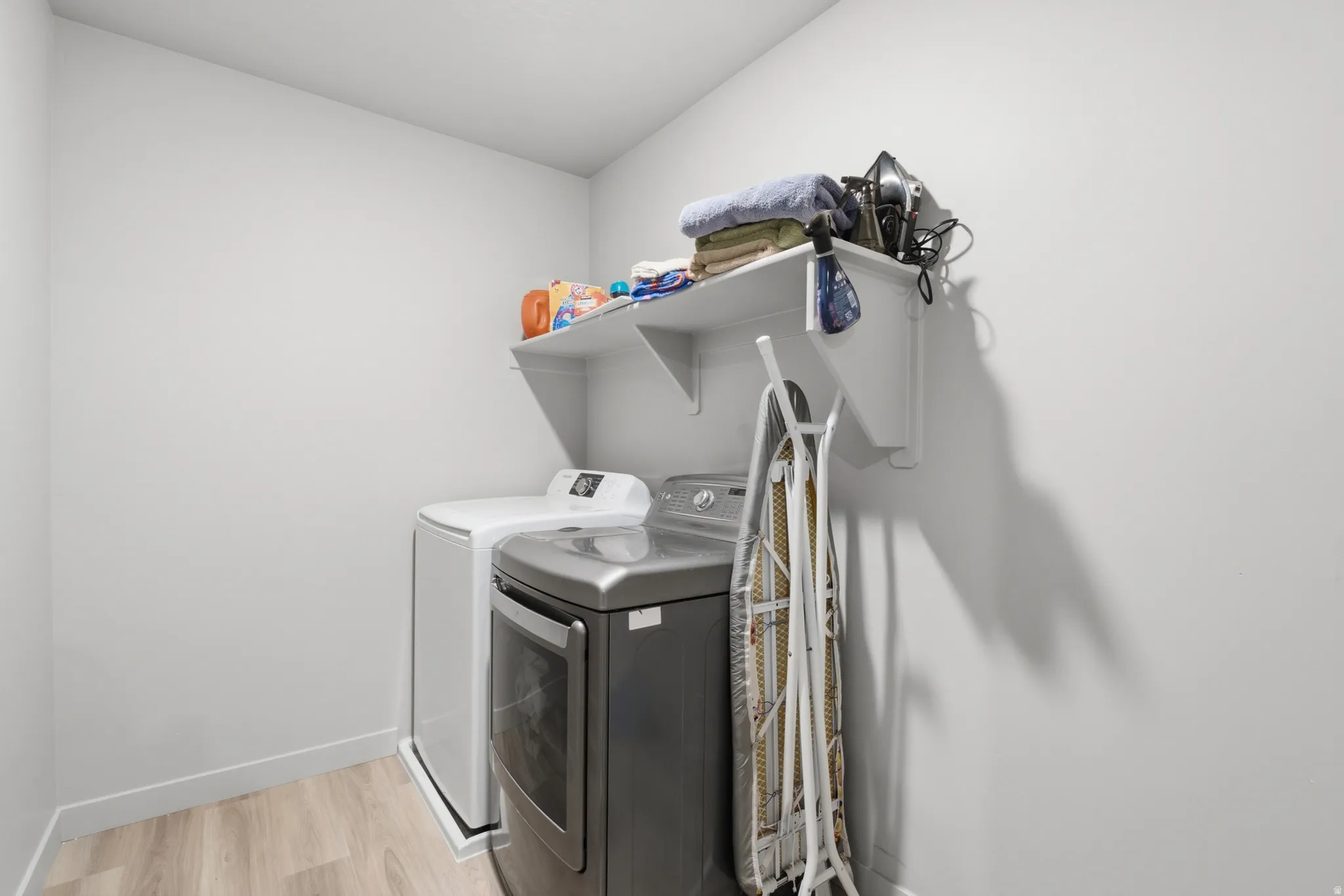 Dedicated laundry space featuring a built-in white wall shelf, light wood-finish flooring, and light gray wall paint