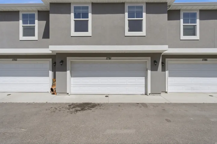 Gray stucco exterior featuring white framed windows with blinds, white garage doors, and exterior lighting fixtures