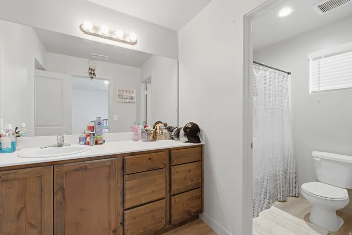 Bathroom vanity featuring a single basin sink, laminate countertop, wood-finish cabinetry with drawers, and a large wall-mounted mirror
