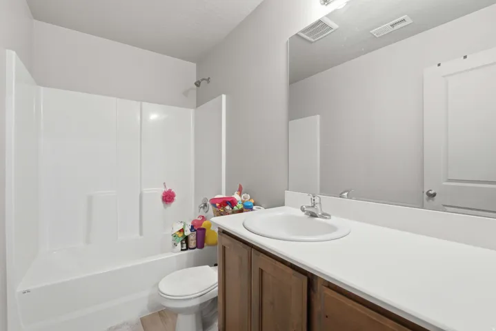 Bathroom featuring a white integrated tub and shower unit, wood-finish vanity cabinetry, a white countertop with an undermount sink, and a large wall-mounted mirror
