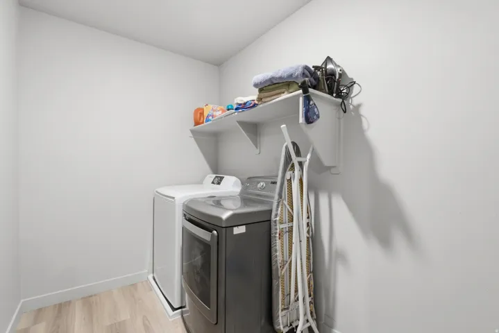 Dedicated laundry space featuring a built-in white wall shelf, light wood-finish flooring, and light gray wall paint