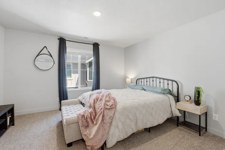 Spacious room featuring neutral carpeting, recessed ceiling lighting, a large window with privacy curtains, and a black metal bed frame
