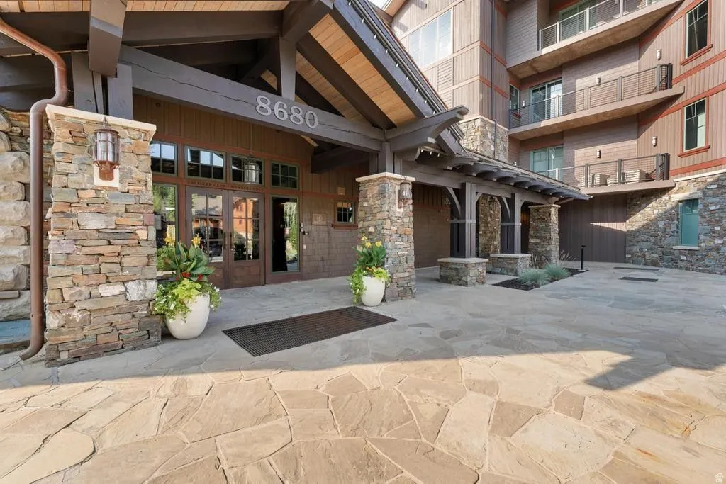 Rustic-inspired building exterior featuring stone cladding, wood siding, a flagstone entryway, exposed wood beams, and a covered portico entrance