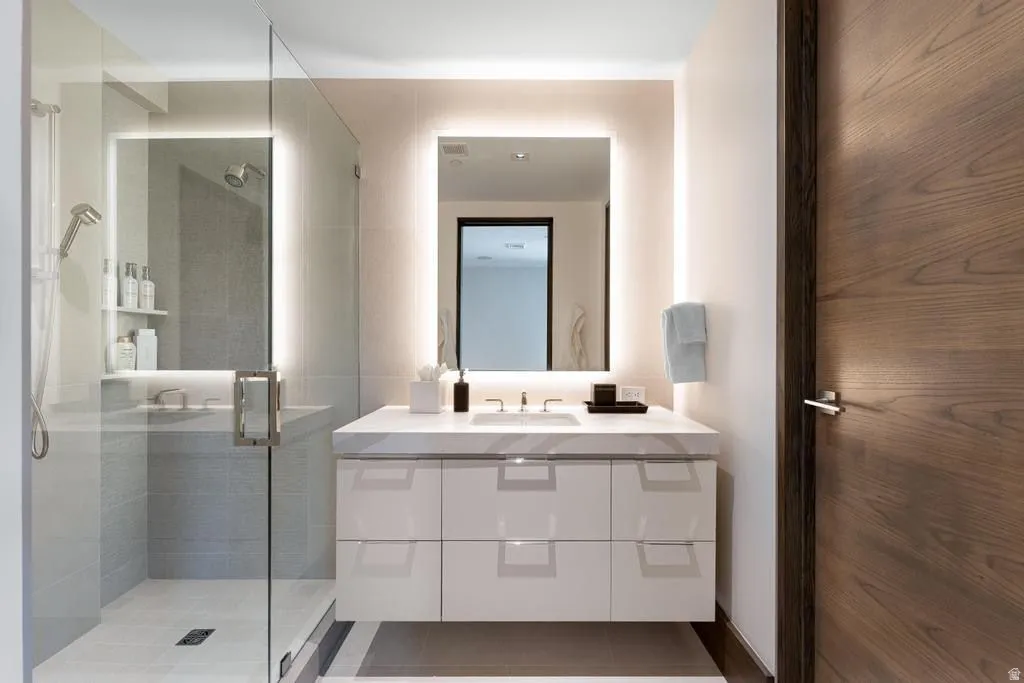 Contemporary bathroom featuring a floating vanity with a white countertop, an illuminated mirror, and a glass-enclosed shower with a built-in niche