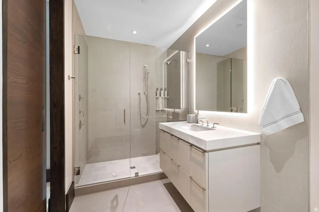 Contemporary bathroom featuring a frameless glass shower enclosure, a vanity with a white countertop, an illuminated mirror, and recessed lighting