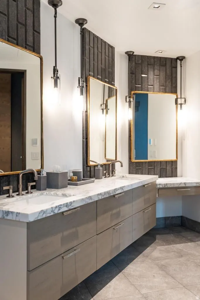 Double vanity featuring a marble-finish countertop with integrated sinks, contemporary cabinetry, and individual wall-mounted mirrors with gold-tone frames