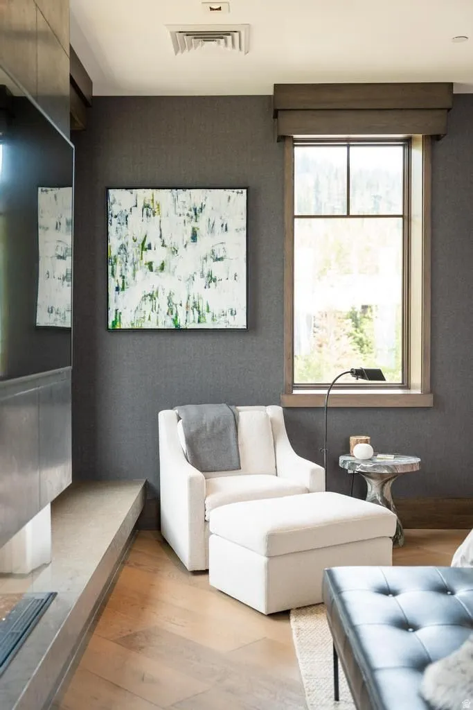 Window with dark wood trim, textured dark gray walls, light wood-finish flooring, and a linear gas fireplace with a concrete hearth