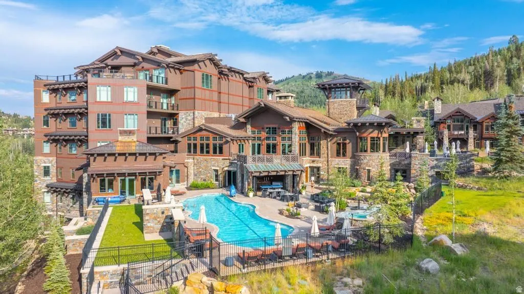 Expansive resort-style property featuring a large outdoor swimming pool, multiple outdoor seating areas, and distinct stone and wood-clad architectural elements
