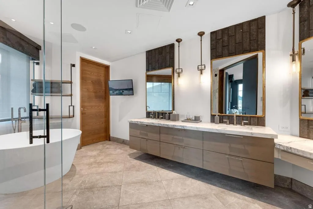 Bathroom featuring a freestanding oval tub, a glass-enclosed shower, a double vanity with stone countertops, and tile flooring