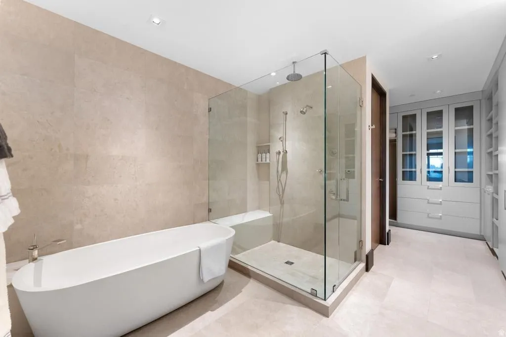 Freestanding soaking tub alongside a glass-enclosed shower with a bench seat and rainfall showerhead