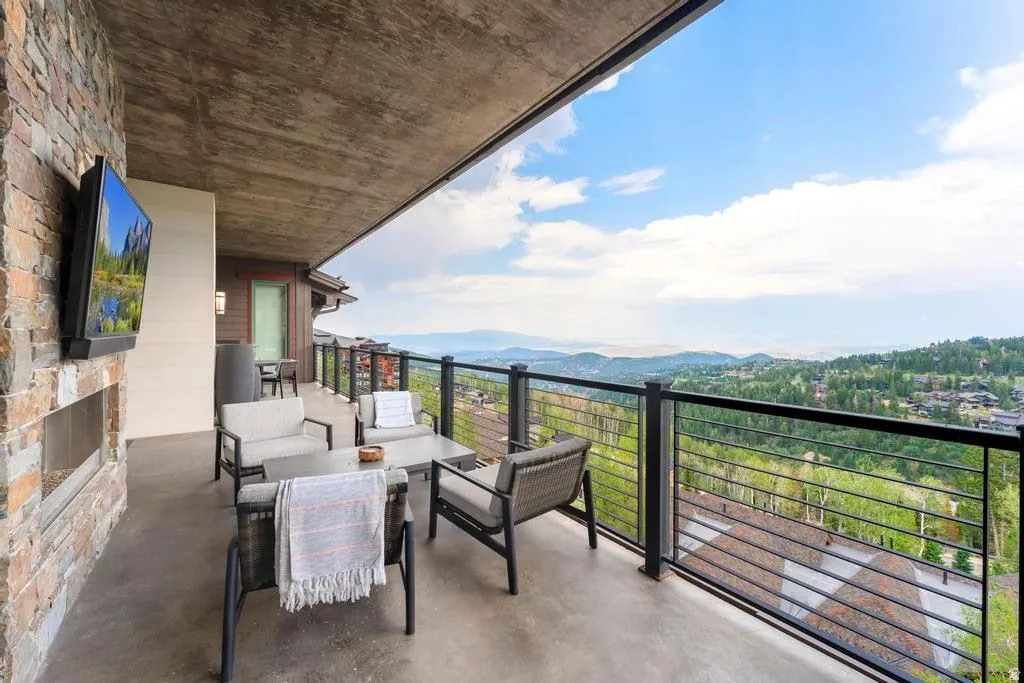 Spacious outdoor patio featuring a stone-clad wall with an integrated outdoor fireplace, a concrete ceiling, and a cable railing system