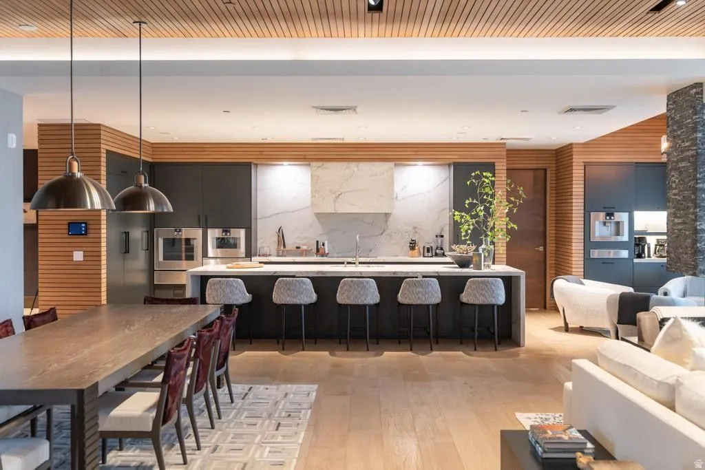 Open-concept living space featuring a gourmet kitchen with integrated appliances, a large center island with seating, a stone slab backsplash, and wood-finish flooring