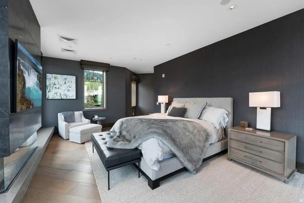 Spacious bedroom featuring dark textured wall coverings, light wood-finish flooring, and a large window with roller shades