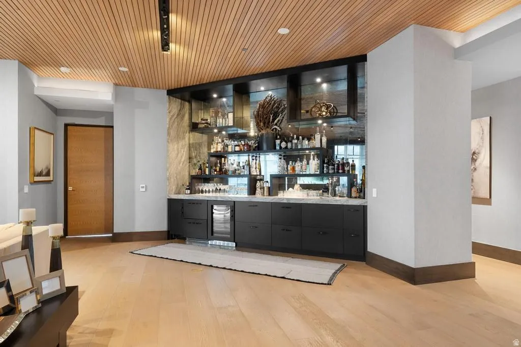 Integrated wet bar featuring black cabinetry, light stone countertop, mirrored backsplash, and built-in beverage cooler