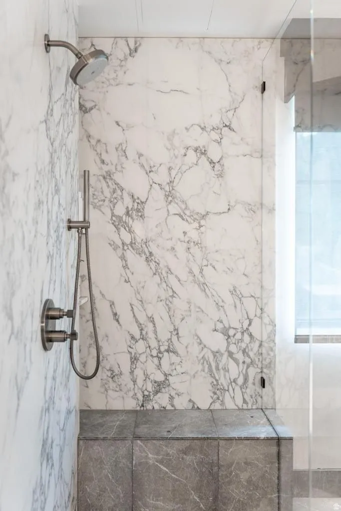 Shower with full-height stone slab surround, brushed nickel fixtures, built-in stone bench, and glass enclosure