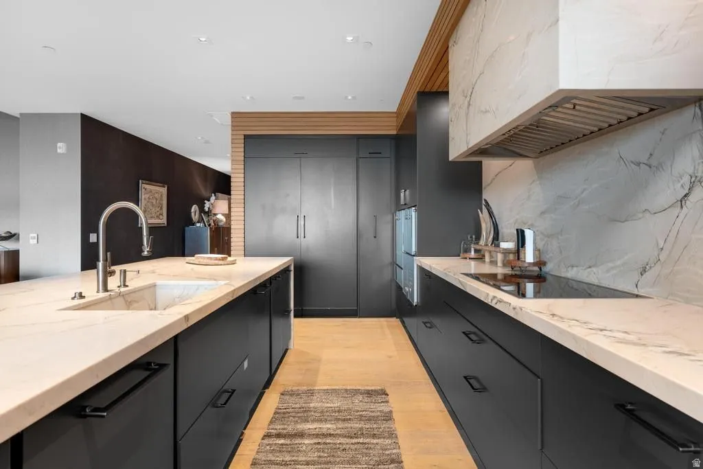 Modern kitchen featuring dark cabinetry, light-toned countertops, integrated appliances, a built-in cooktop, and a matching stone backsplash