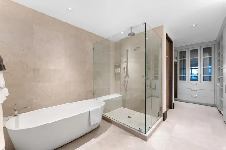 Freestanding soaking tub alongside a glass-enclosed shower with a bench seat and rainfall showerhead