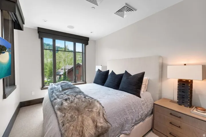 Large multi-pane window with dark trim, recessed ceiling lighting, wall-mounted television, built-in ceiling speaker, and light-toned carpeting