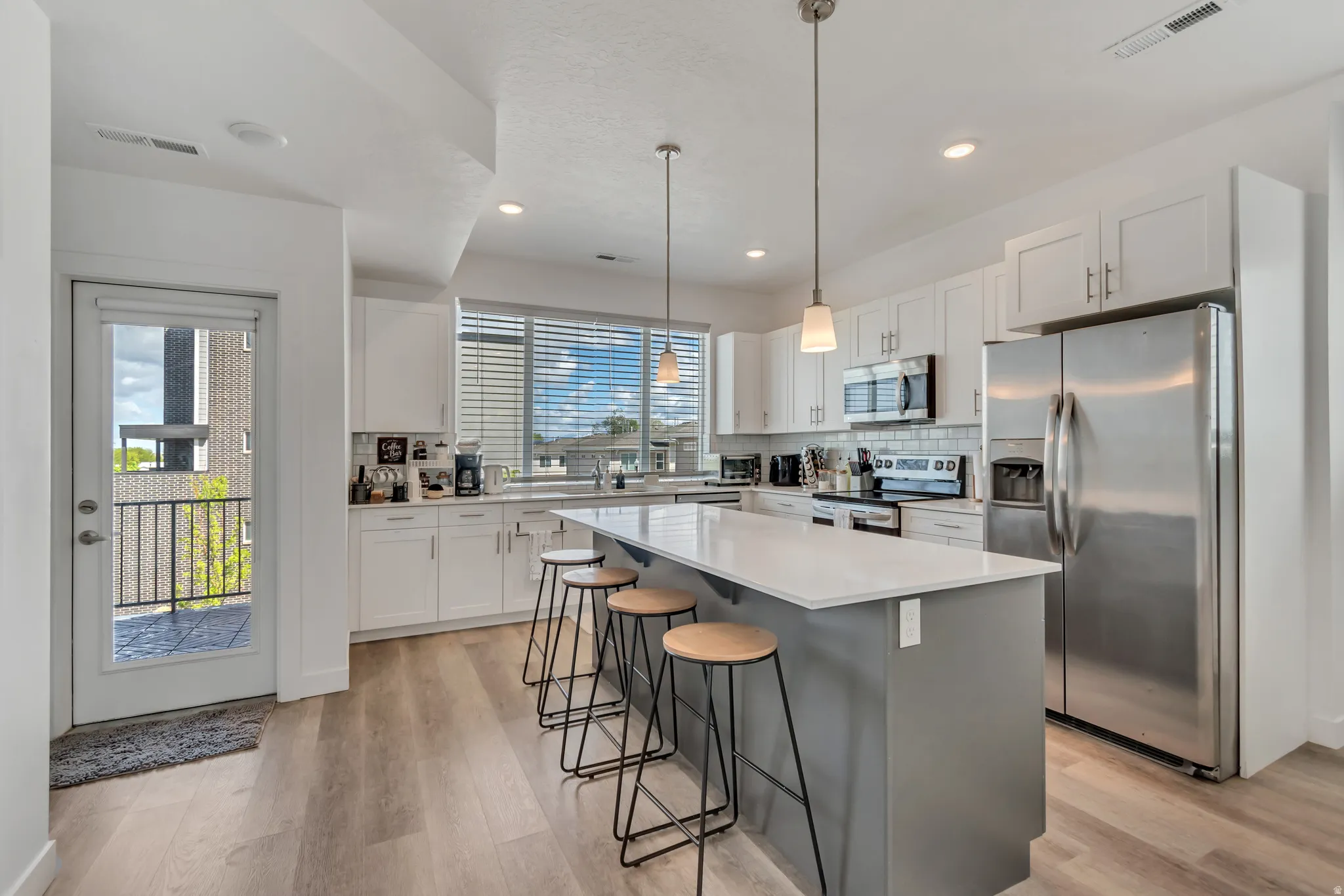Modern kitchen featuring a large central island with seating, white shaker cabinetry, stainless steel appliances, and wood-finish flooring
