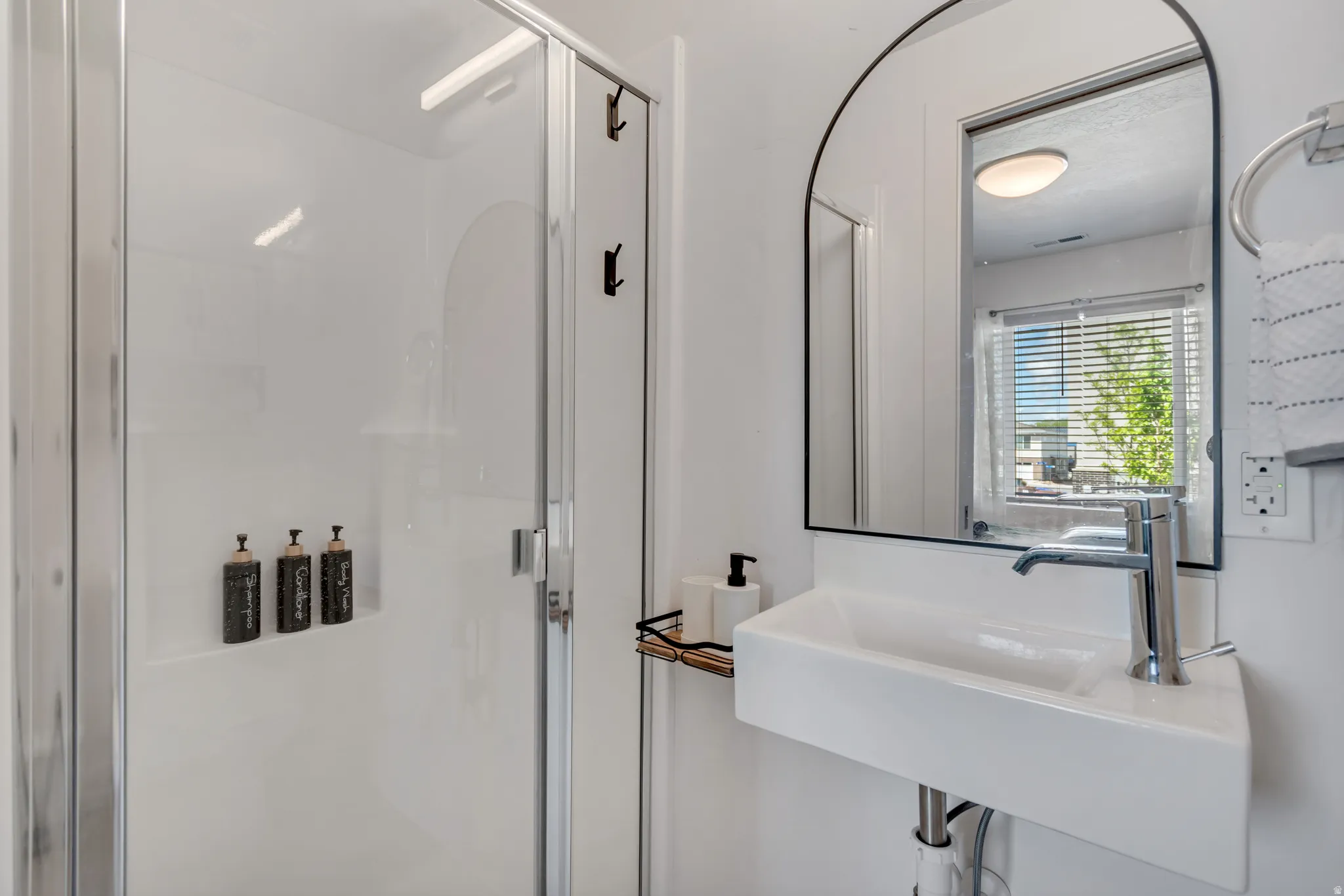 Contemporary bathroom featuring a glass-enclosed shower with integrated shelving, a rectangular vessel sink with chrome faucet, and an arched wall mirror