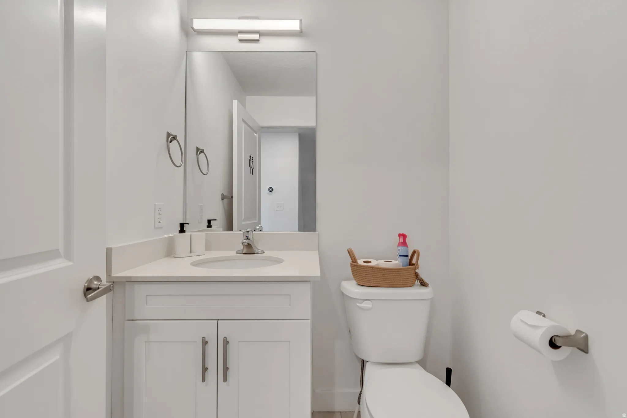 Powder room featuring a white single-sink vanity with a light-toned countertop, a rectangular mirror, and a wall-mounted light fixture