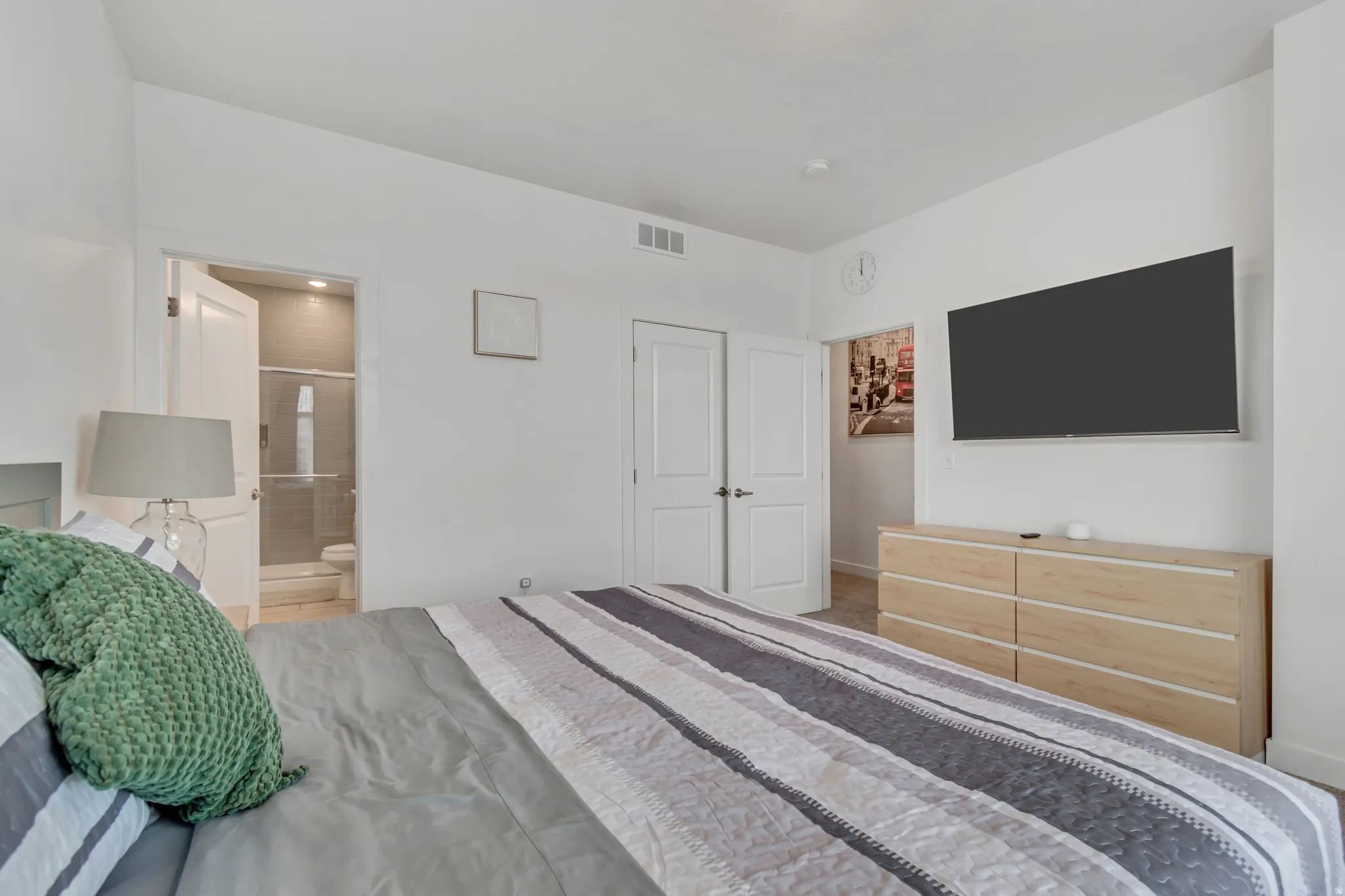 Bedroom interior featuring a neutral color palette, carpet flooring, a wall-mounted entertainment area, and an en-suite bathroom with a glass-enclosed shower