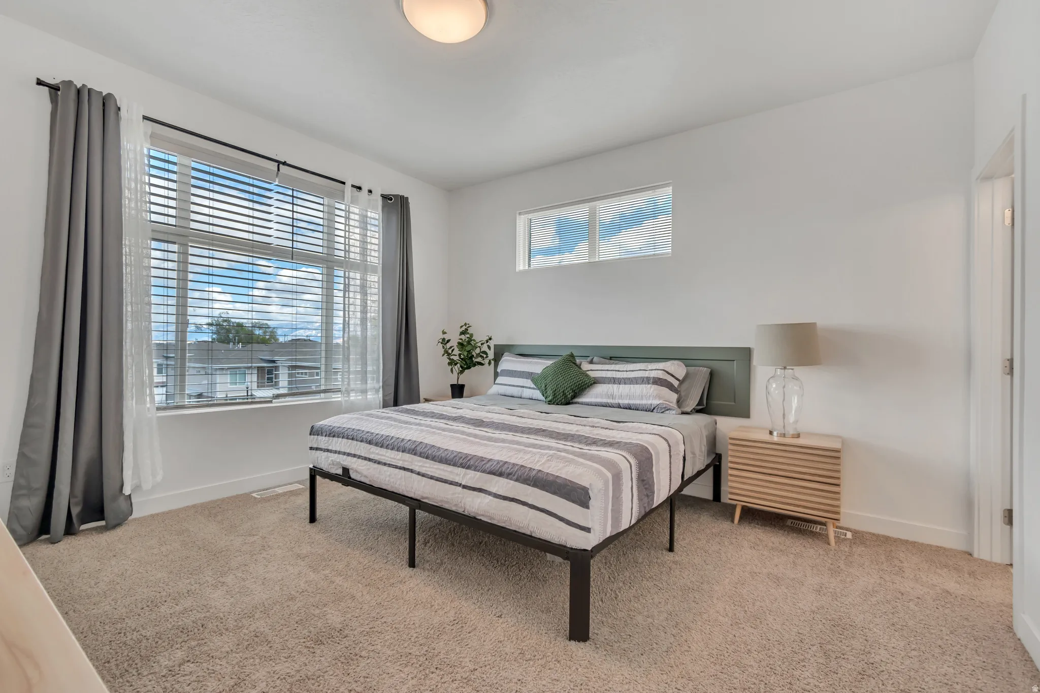 Bedroom featuring light tan carpet flooring, a large window with blinds, and a high horizontal window