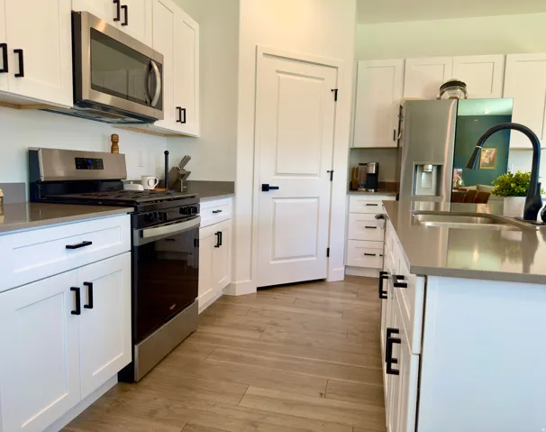 Modern kitchen featuring white shaker cabinetry, stainless steel appliances, light-toned countertops, wood-finish flooring, and a kitchen island with a built-in sink