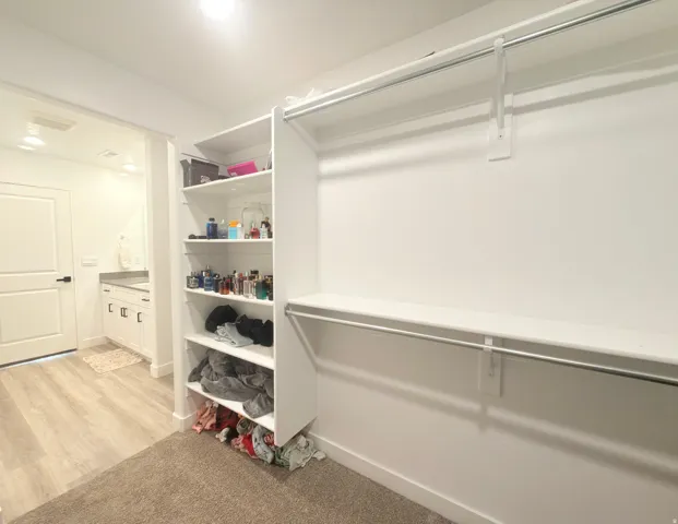 Spacious walk-in closet featuring white built-in shelving, chrome hanging rods, and an adjacent bathroom entry