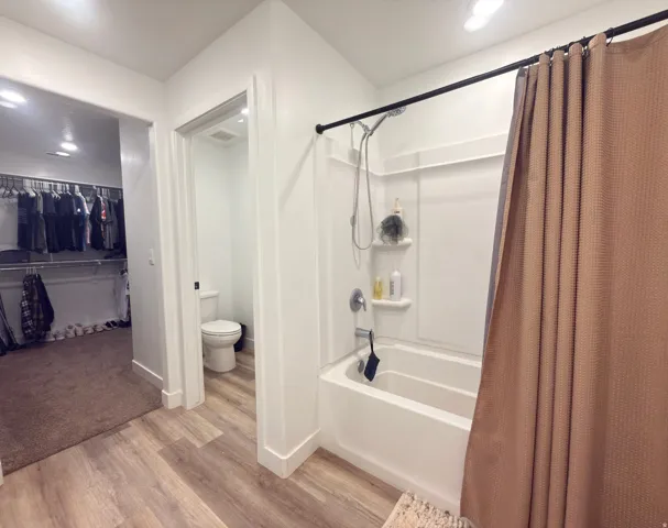 Full bathroom featuring a white tub/shower combination with integrated shelving, chrome fixtures, and wood-finish flooring