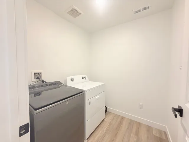 Dedicated laundry area featuring wood-finish flooring, white walls, and a ceiling-mounted ventilation system