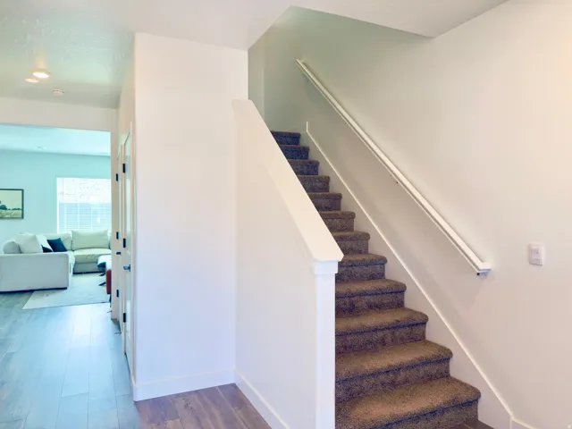 Carpeted staircase featuring a white handrail and a painted wood newel post
