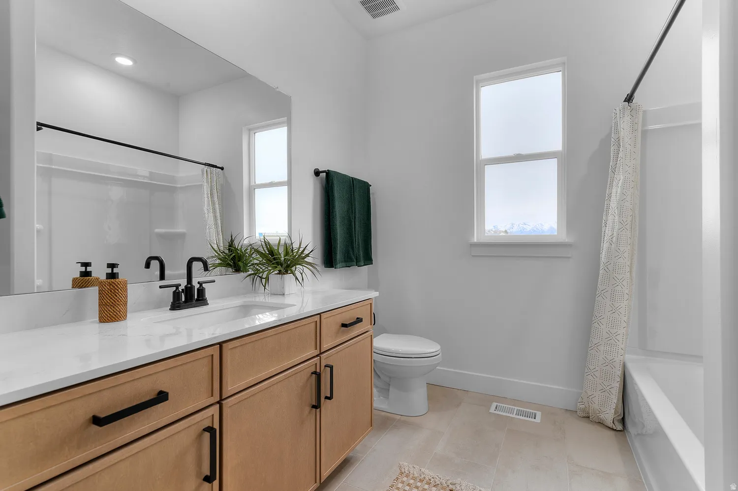 Bathroom featuring a double-sink vanity with light wood-finish cabinetry, white countertop, and matte black fixtures