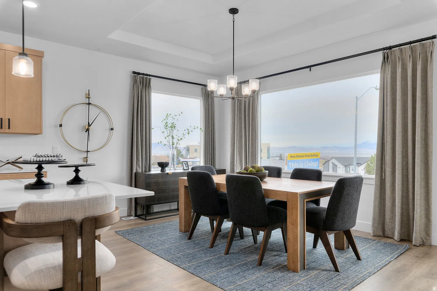 Open-concept dining area featuring an elegant chandelier, large windows with expansive outdoor scenery, a tray ceiling, and light wood-finish flooring