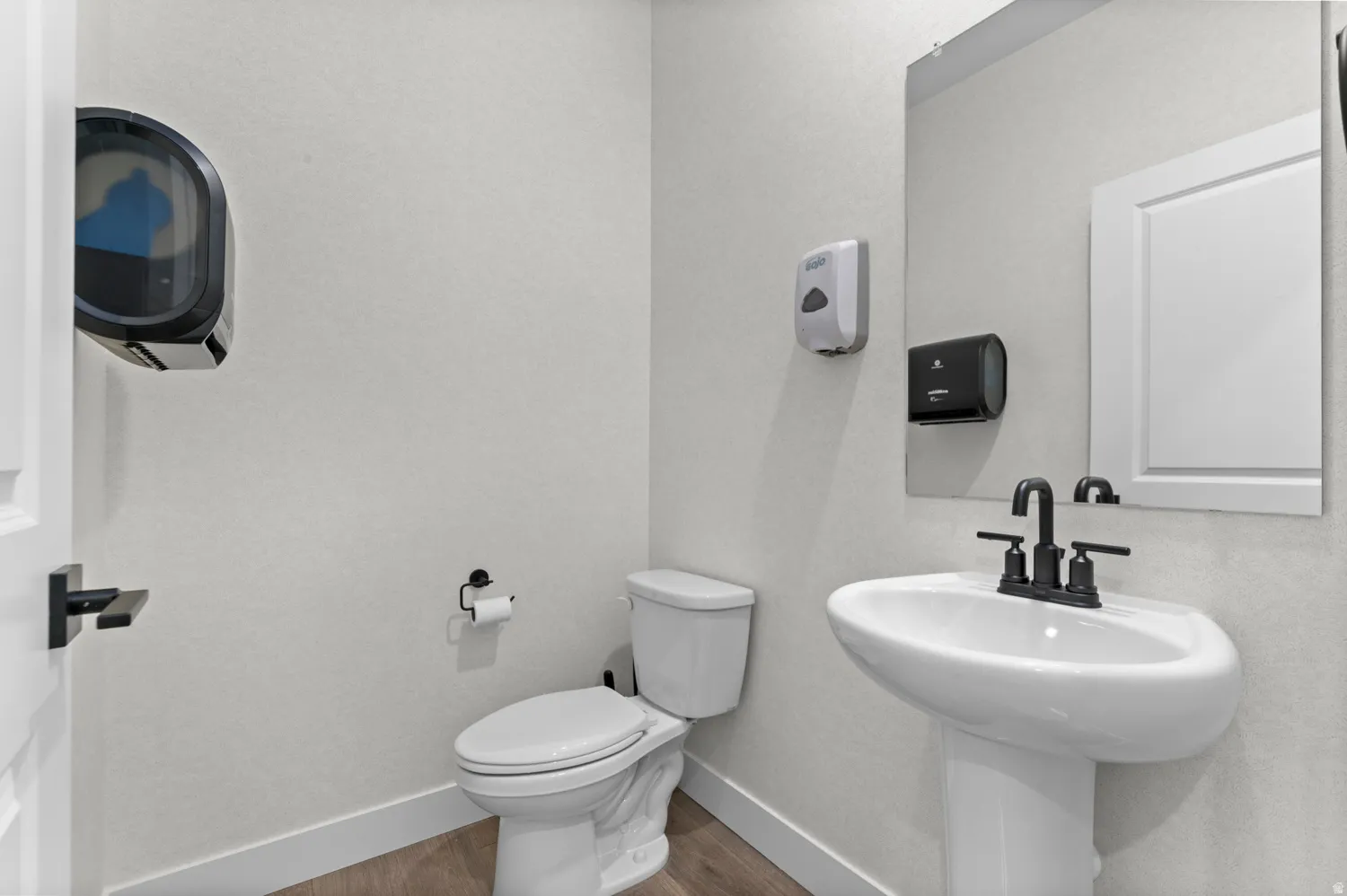 Pedestal sink with matte black faucet, wall-mounted mirror, and wood-finish flooring