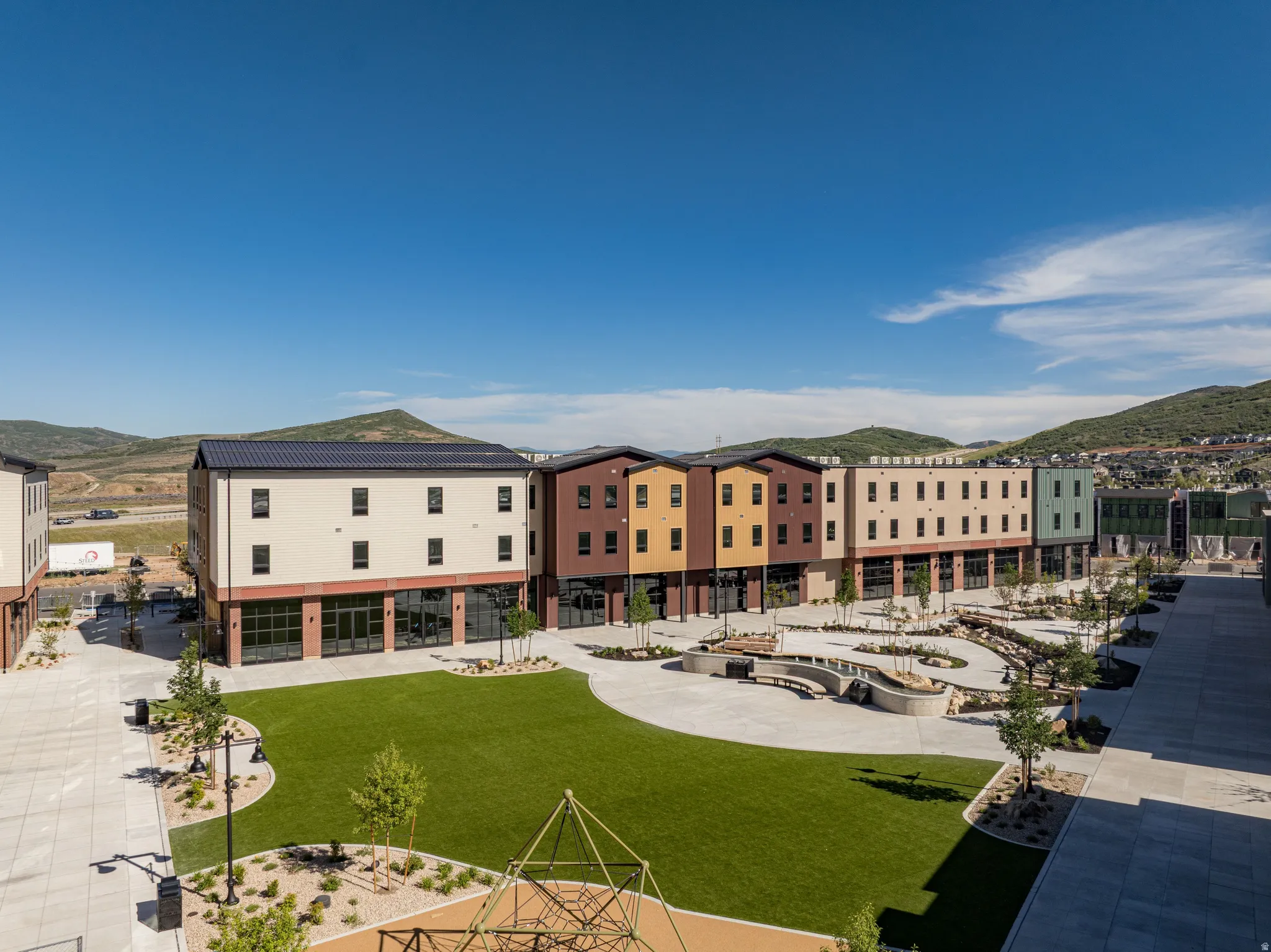 Central green space featuring artificial turf, mature trees, and a geometric play structure