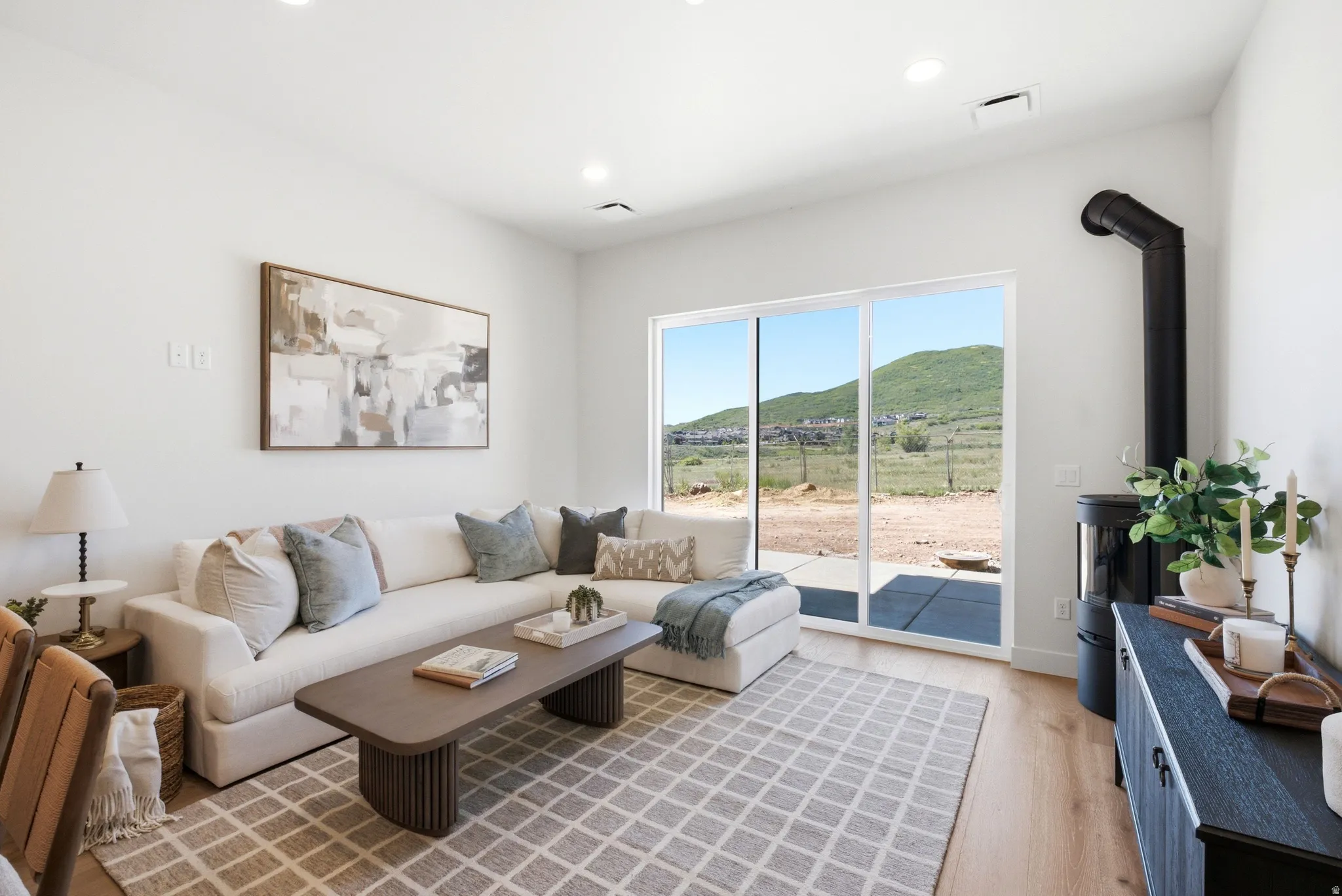 Living area featuring a floor-to-ceiling sliding glass door, a contemporary wood-burning stove, wood-finish flooring, and recessed lighting