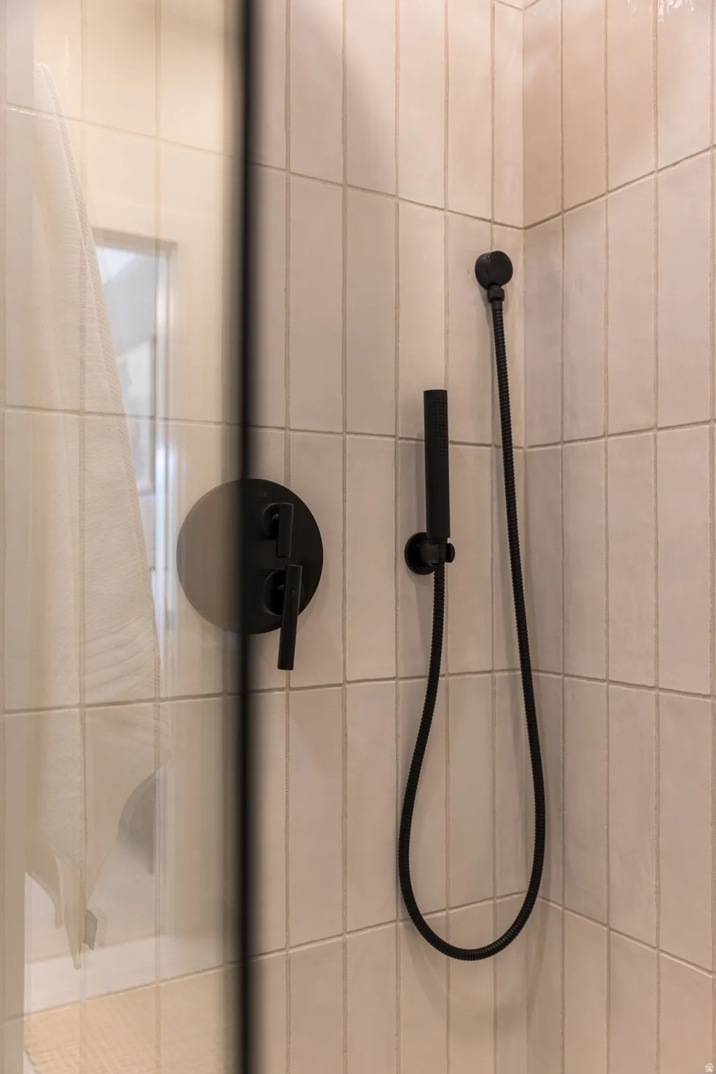 Shower enclosure featuring matte black fixtures, a handheld showerhead, and vertically stacked rectangular wall tiles