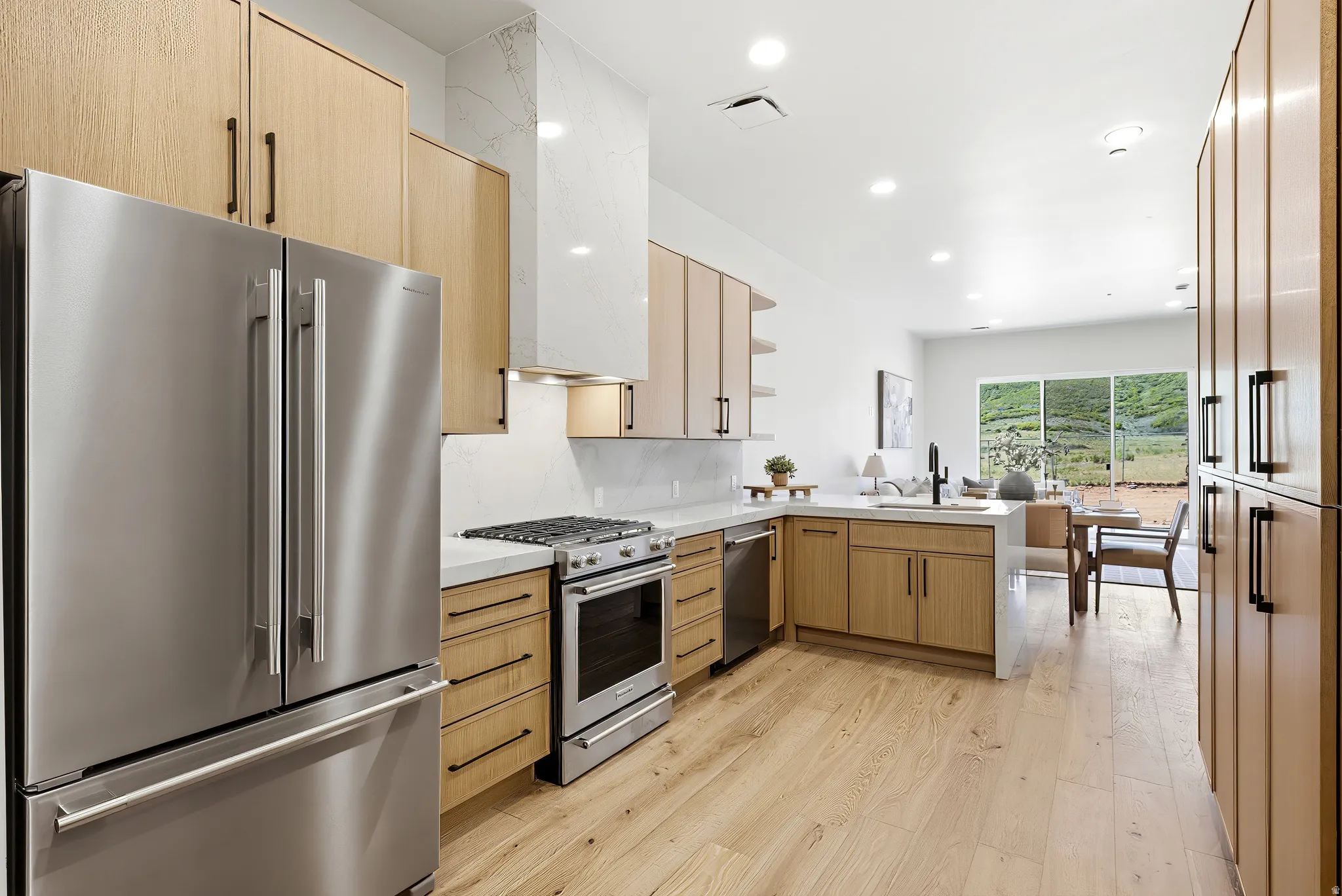 Modern kitchen featuring light wood-finish cabinetry, stainless steel appliances, a gas range, white countertops, and wood-finish flooring