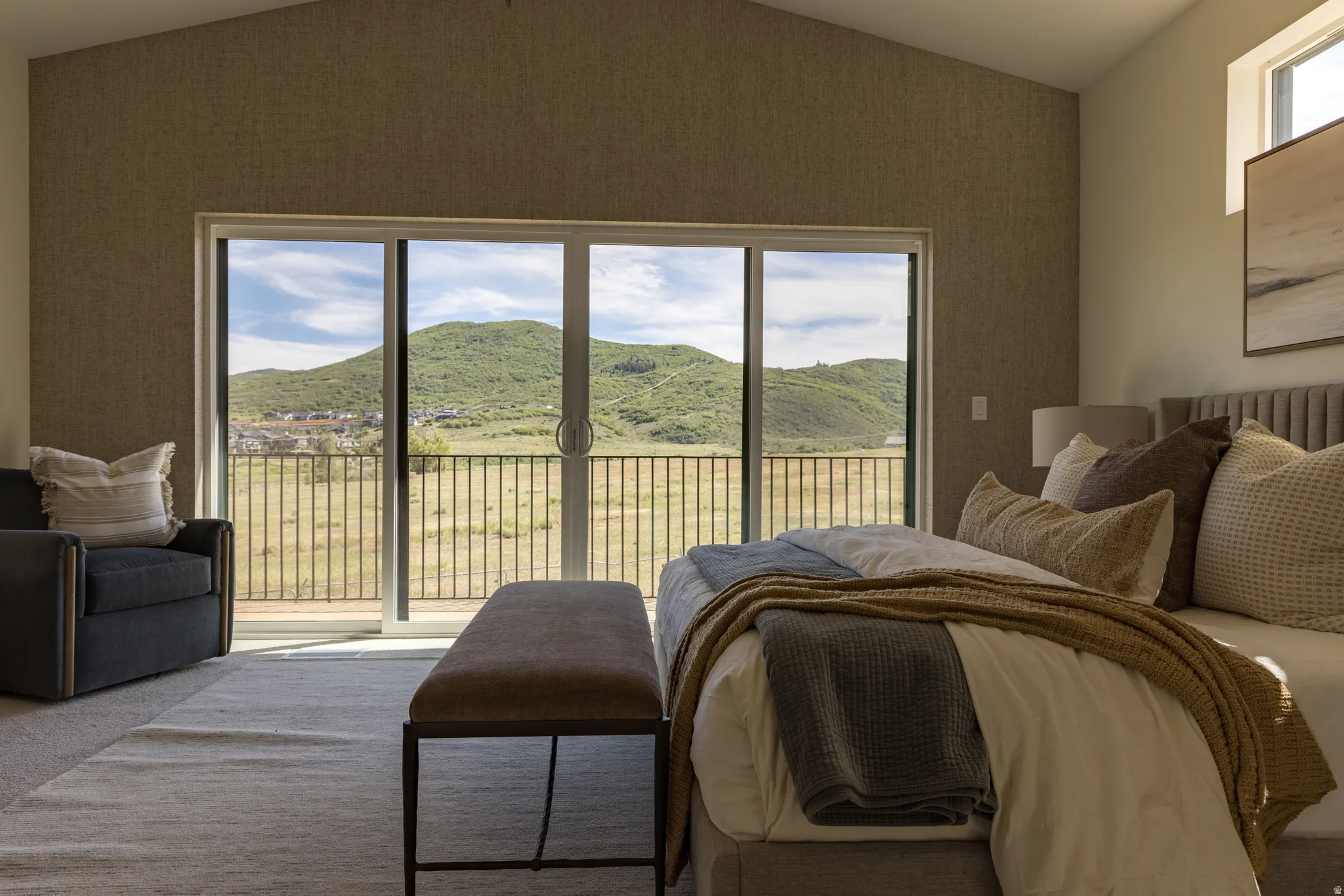 Sliding glass doors opening to a metal railing balcony, with a vaulted ceiling and textured accent wall