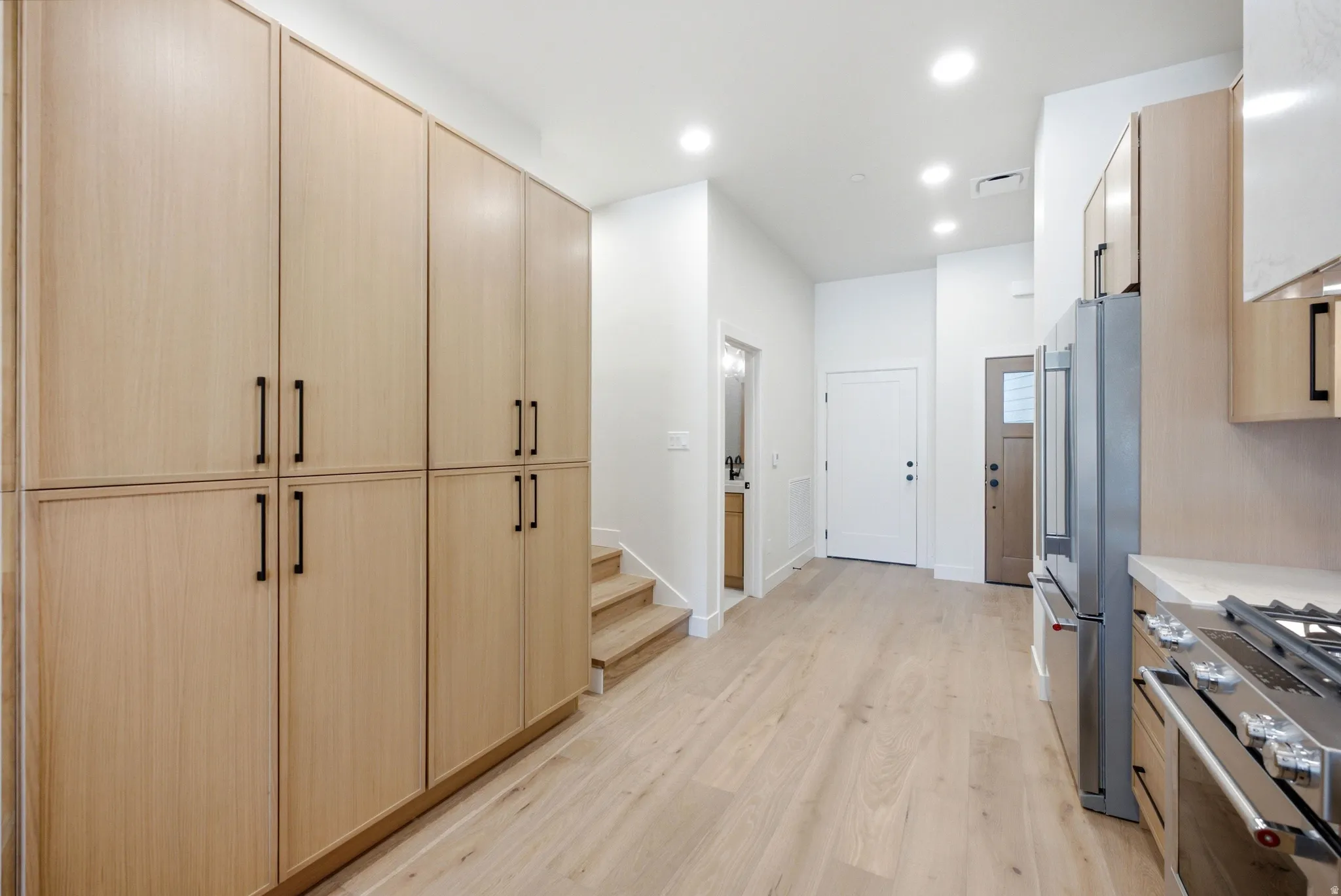 Full-height wood-finish cabinetry with black hardware, wood-finish flooring, recessed lighting, and stainless steel appliances