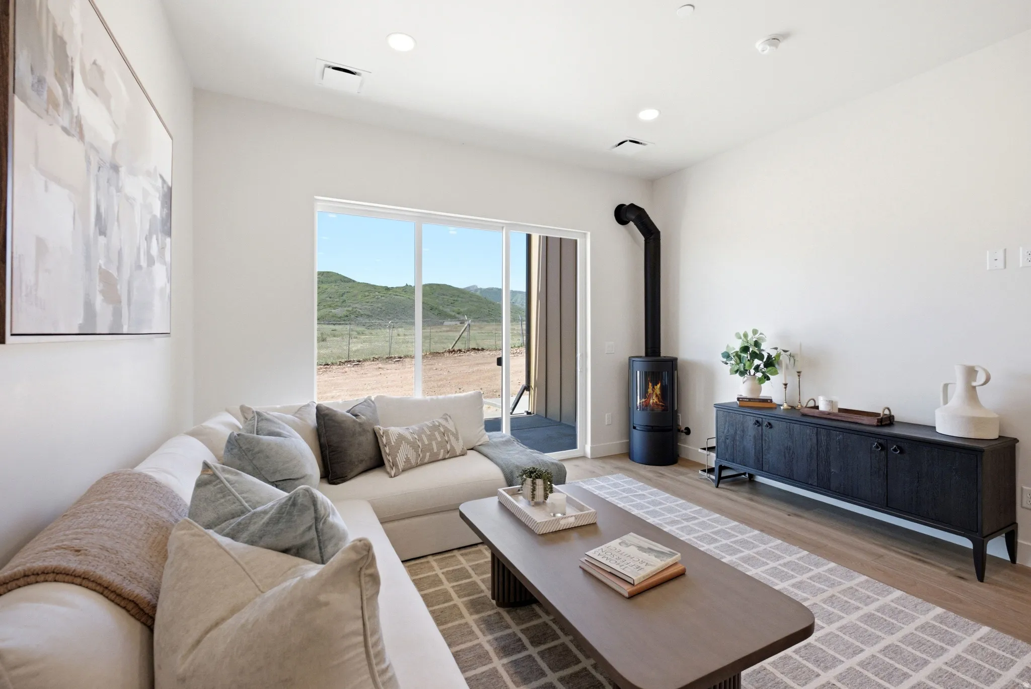Bright living area featuring wood-finish flooring, a modern wood-burning stove, recessed lighting, and a sliding glass door opening to a mountainous landscape