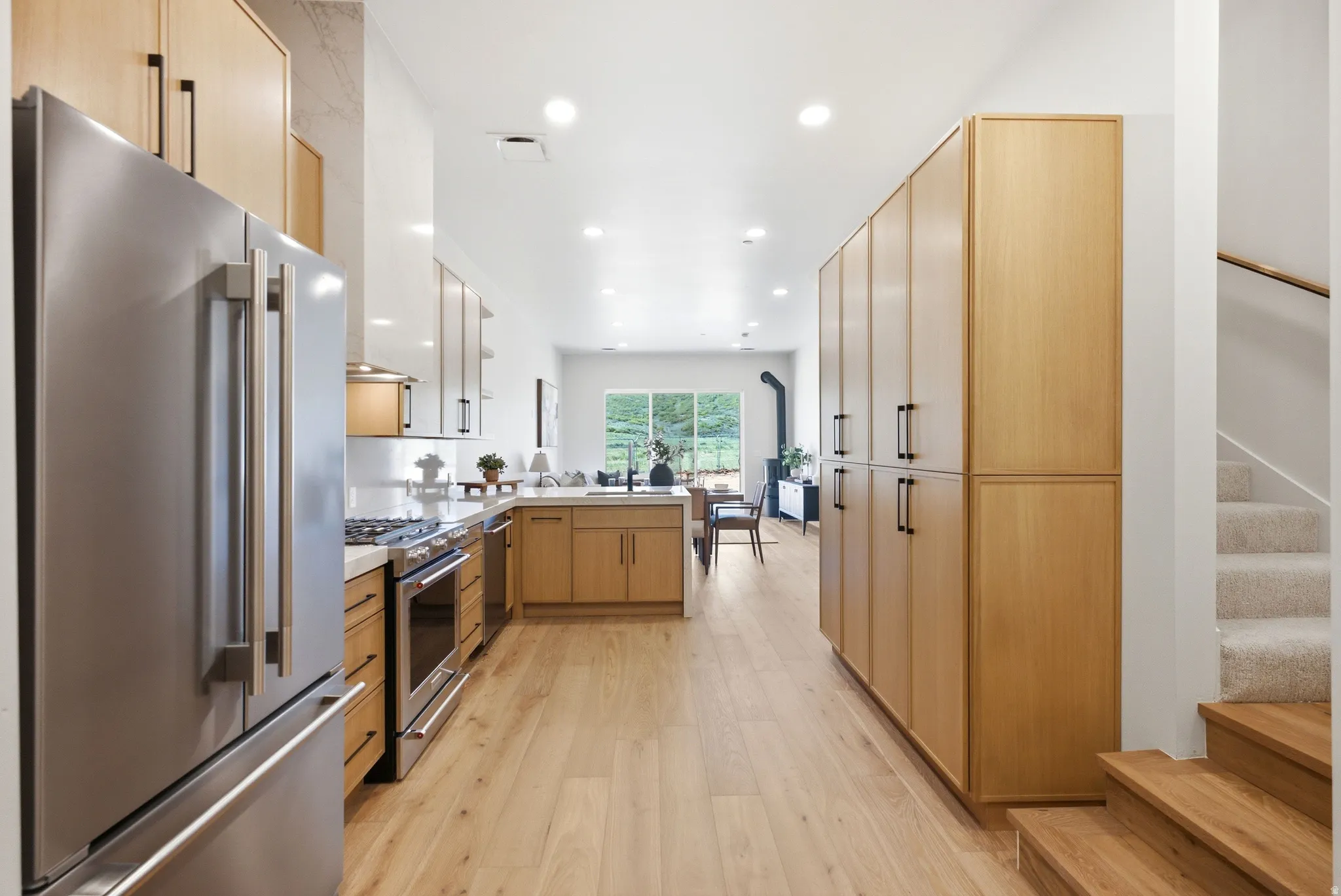 Expansive kitchen with wood-finish flooring, light wood cabinetry, stainless steel appliances, and a built-in kitchen island